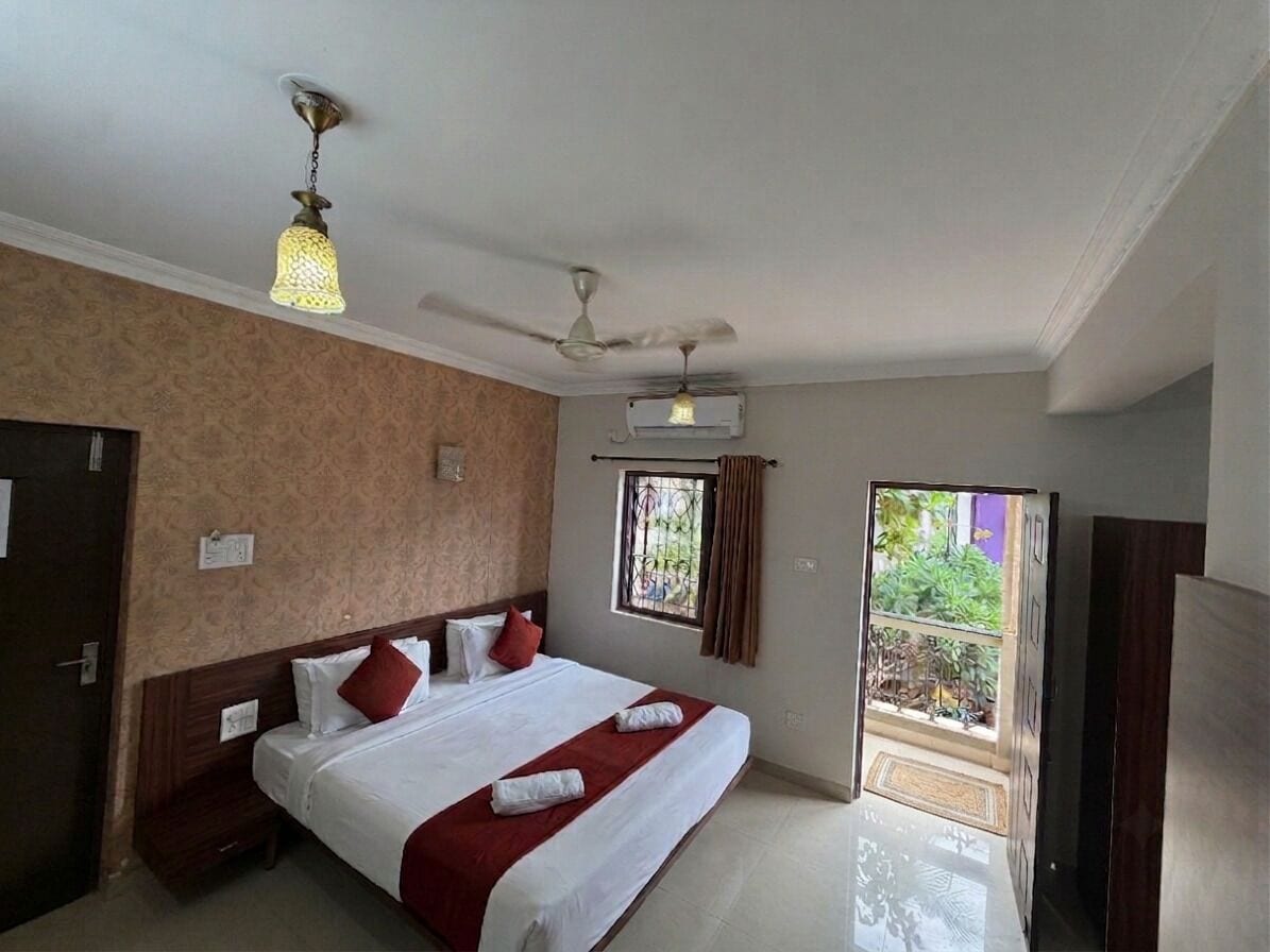 A hotel room with a bed, ceiling fan, air conditioning unit, and a view of the outdoors.