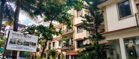 A multi-story building with balconies, surrounded by lush greenery and palm trees.
