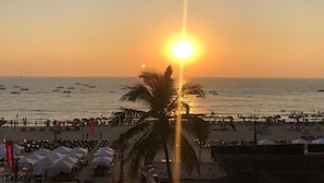 Escena de playa con atardecer, palmeras y sombrillas.