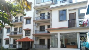 Un edificio residencial de varios pisos con balcones, un camino de entrada pavimentado y una pequeña área ajardinada.