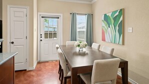 A dining area with a wooden table, white chairs, a vase with flowers, and a painting on the wall. - SD2 • Spacious Family Townhome•3BR• Backyard• Fast Wi-Fi (Selma)