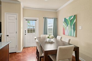 A dining area with a wooden table, white chairs, a vase with flowers, and a painting on the wall. - SD2 • Spacious Family Townhome•3BR• Backyard• Fast Wi-Fi (Selma)