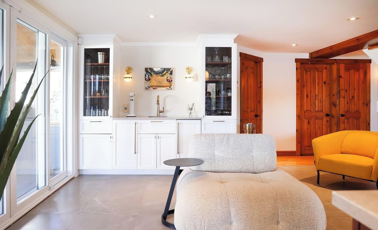 A modern kitchen with white cabinetry, a dining area with a round table and a yellow armchair, and a large wooden door.