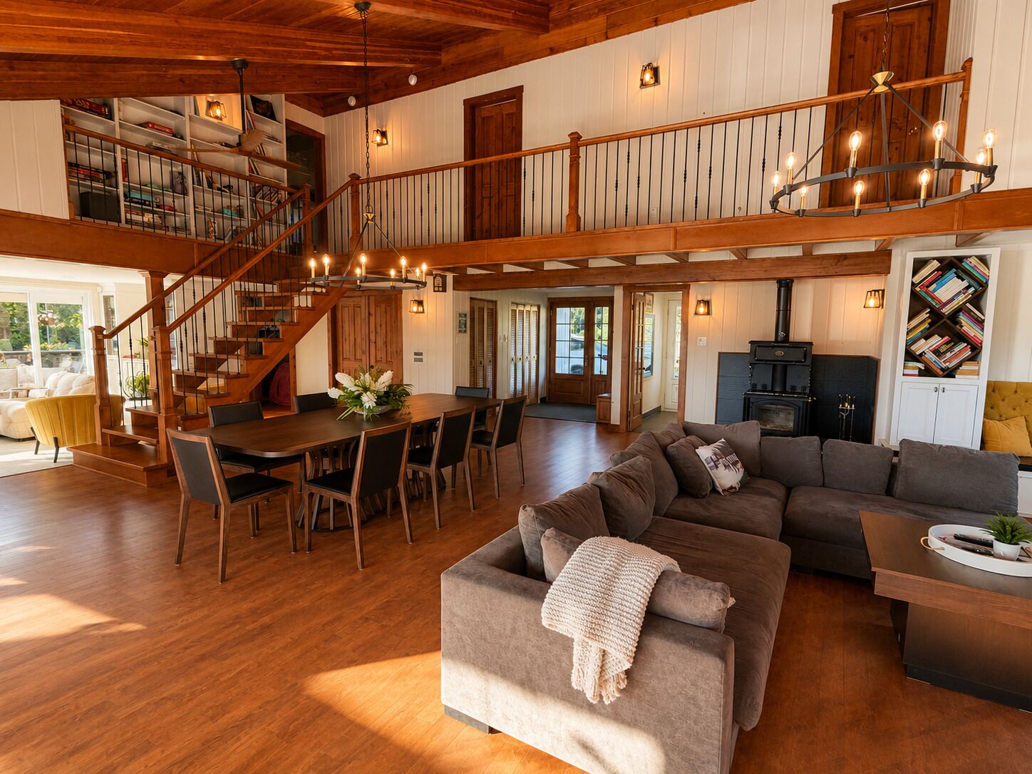 A spacious living area with a wooden staircase, a dining table, and a cozy seating arrangement.