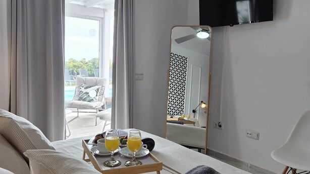 Hotelkamer met een bed, een nachtkastje met een ontbijttafel, een plafondventilator, een aan de muur bevestigde televisie en uitzicht op het buitengebied.