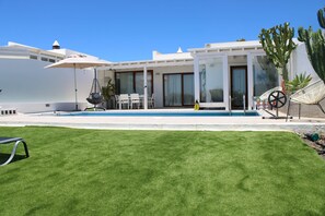 Ein modernes Haus mit Swimmingpool, einer Terrasse mit Stühlen und einer Kakteenpflanze.