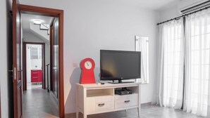 A room with a television on a stand, a clock, and a view of a hallway with a red cabinet. - Luxury villa with a stunning sea view (Playa Blanca)