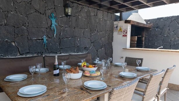 An outdoor dining area with a stone wall, a grill, and a table set for four. - Luxury villa with a stunning sea view (Playa Blanca)