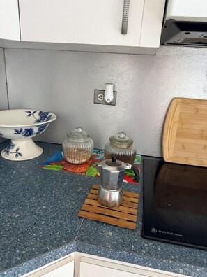 Eine Küchenarbeitsplatte mit einer Kaffeemaschine, zwei Glasbehältern, einer Blumen-Schale und einer farbenfrohen Tischmatte.