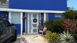 A two-story building with a blue exterior, a garage door, and a driveway leading to a front porch with a bench and potted plants. - Studio apartment 7 minutes from the airport in Carolina (Carolina)