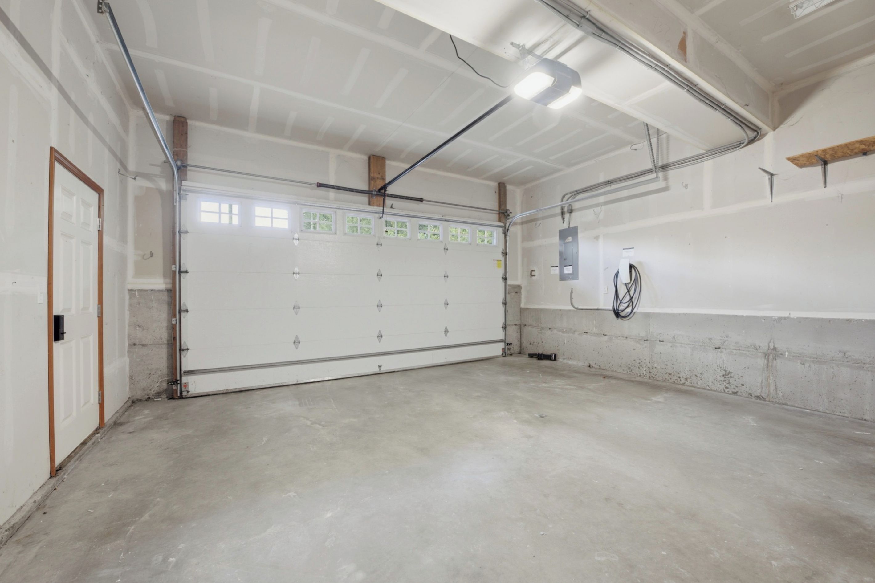 A large, empty garage with a concrete floor, a white garage door, and a metal ceiling with exposed beams.