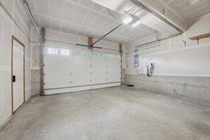 Eine große, leere Garage mit Betonboden, einer weißen Garagentür und einer Metalldecke mit freiliegenden Balken.