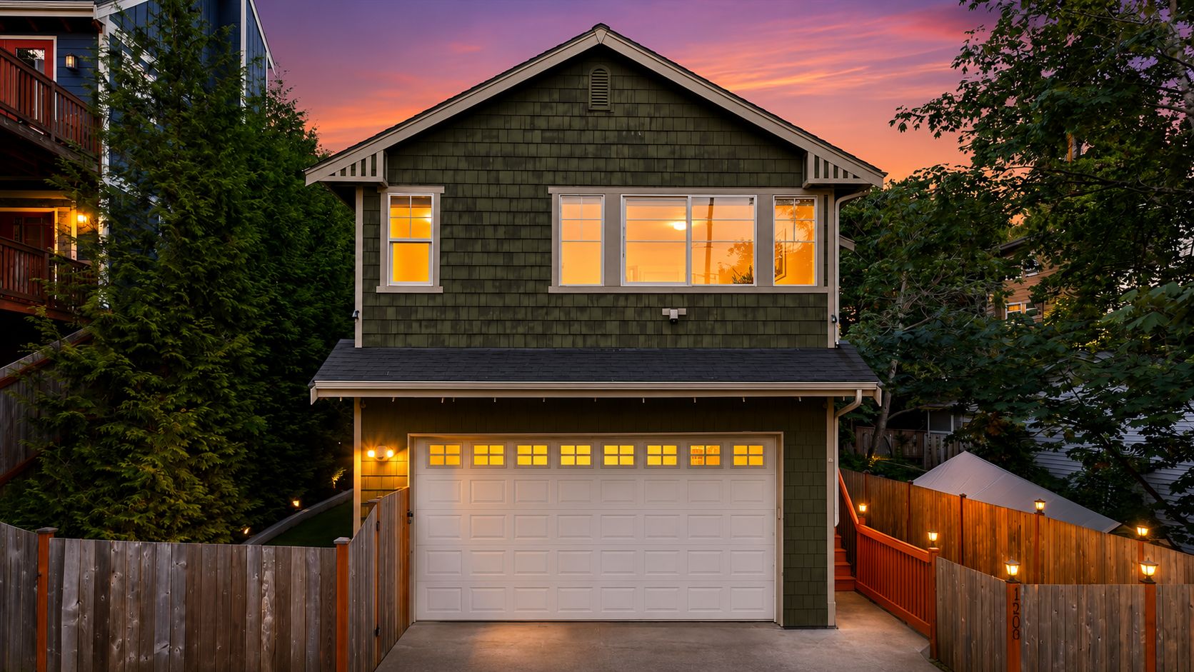 A two-story house with a garage, wooden fence, and a porch with lights.