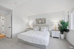 Un dormitorio con una cama grande, dos mesitas de noche con lámparas, una obra de arte en la pared y una planta en maceta.
