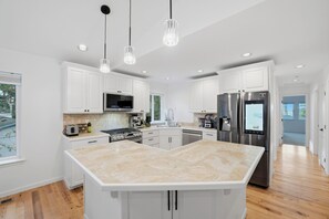 A modern kitchen with white cabinetry, stainless steel appliances, and a large island. - Peek-a-boo Lake/Mountain | 4BR + Office/Gym | Turf (Sammamish)