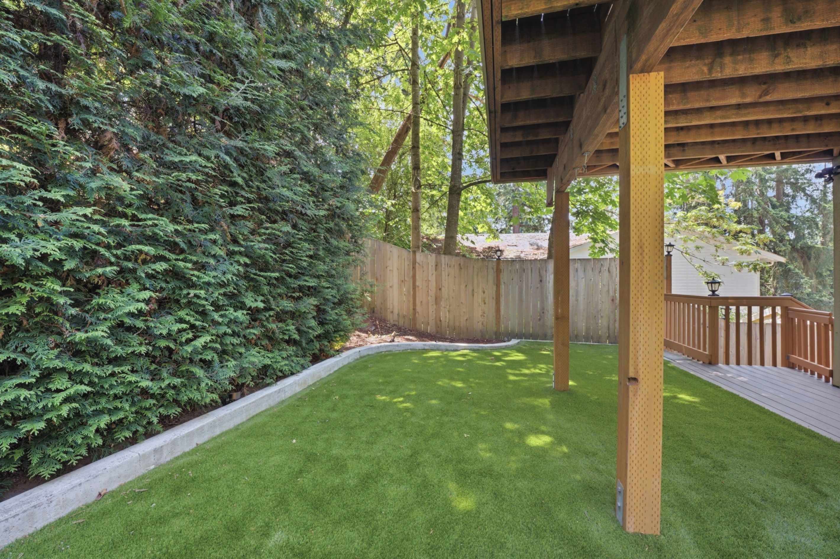 A well-maintained backyard with a wooden deck, a fenced area, and a lawn.