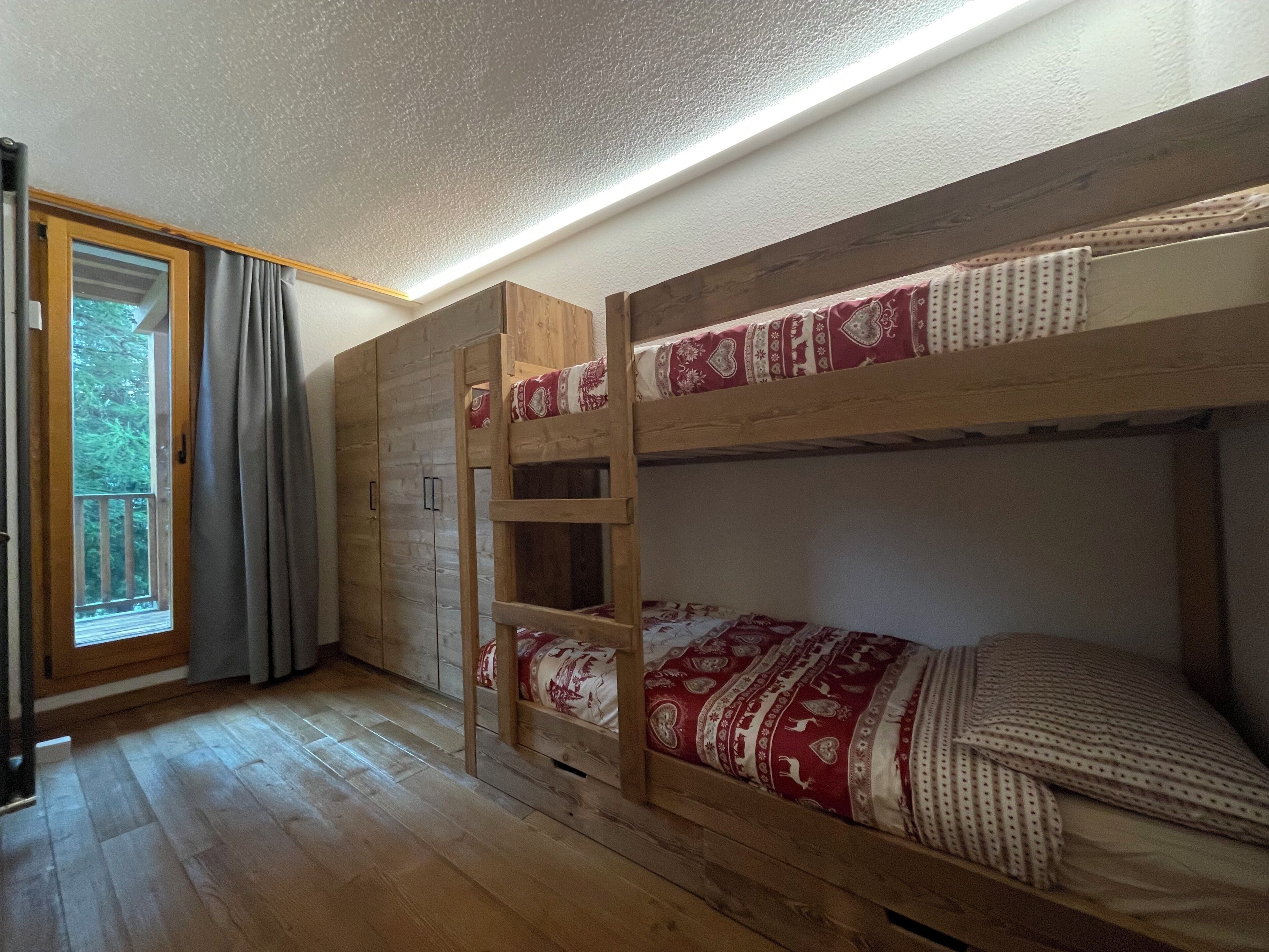 Un lit superposé avec une échelle, une armoire et une porte-fenêtre coulissante donnant sur un balcon.