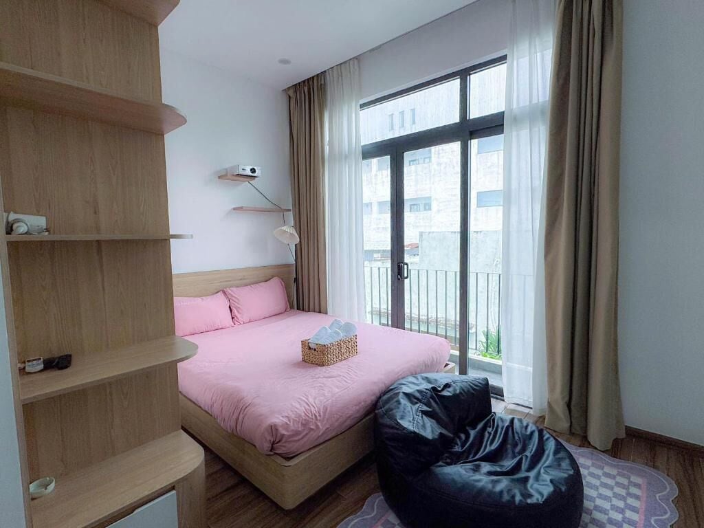 Un dormitorio moderno con cama, sillón de plumas, estantería y ventana con cortinas.