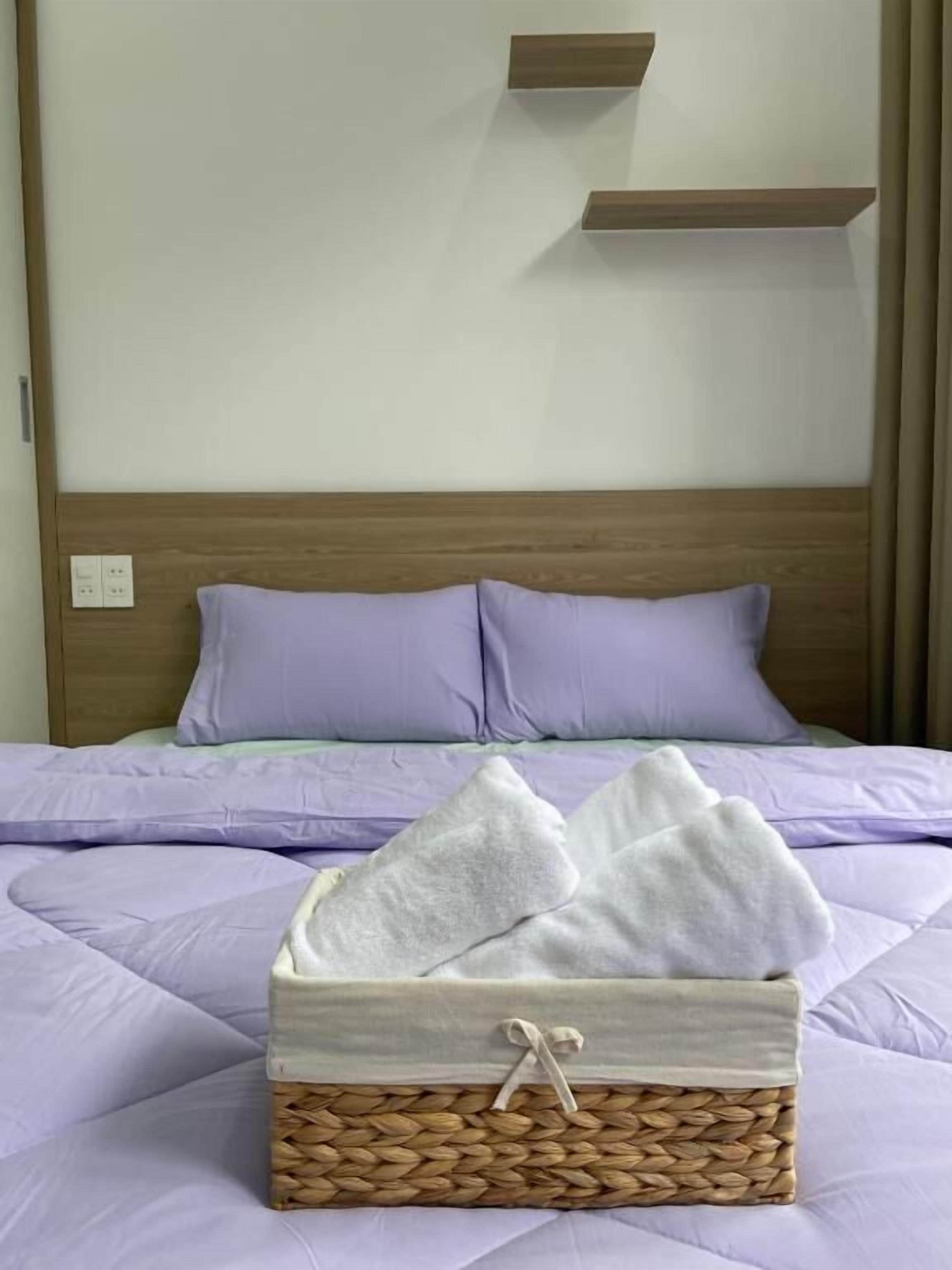 Una cama con cabecera, una mesita de noche y una cesta con toallas.