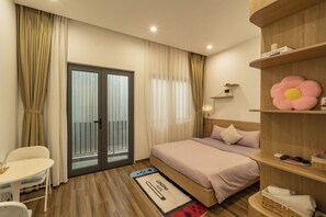 Habitación de hotel con cama, escritorio, silla, estante de madera con decoración floral y puerta de vidrio corredera.
