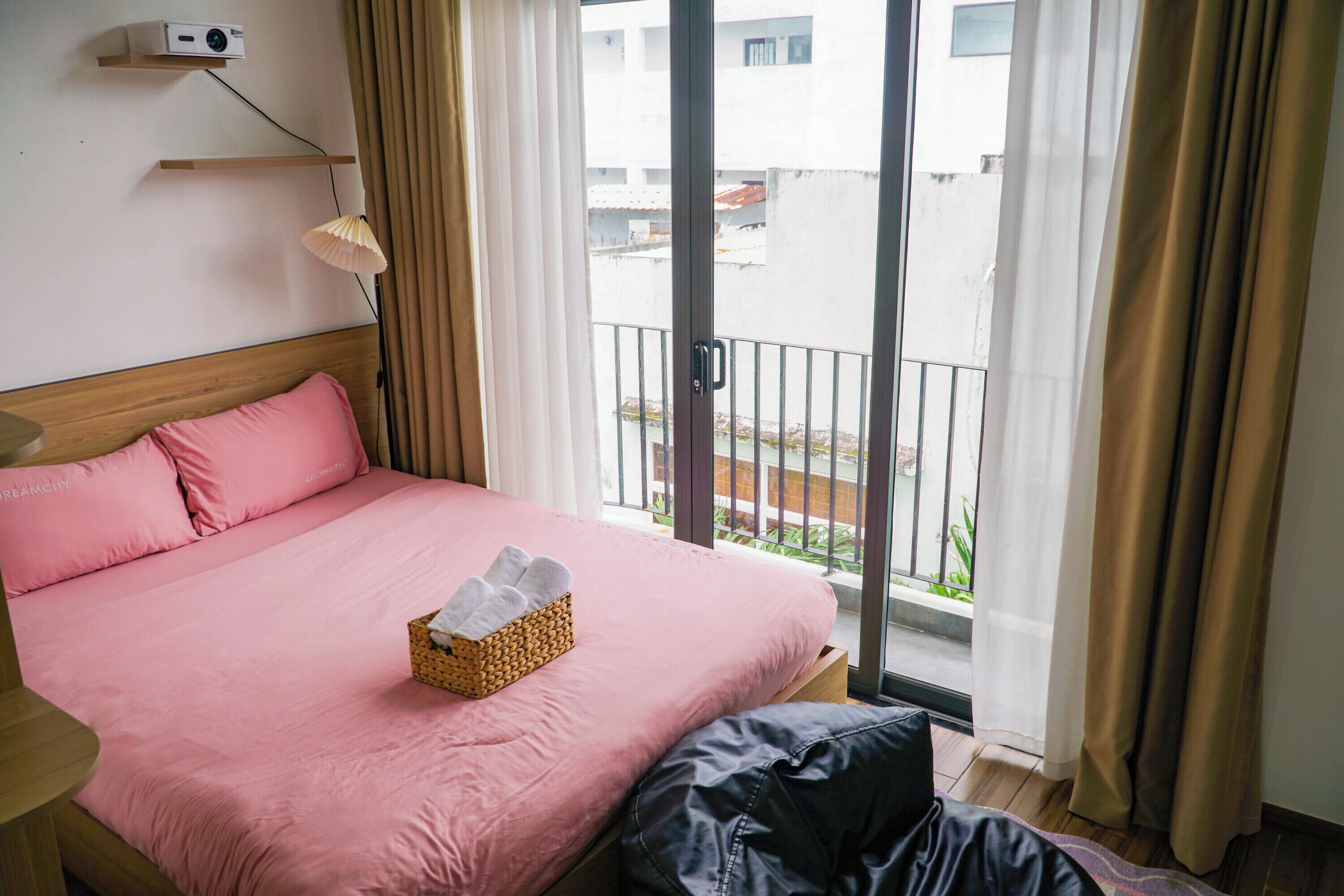 A hotel room with a bed, a bedside table, a lamp, and a view of the outside.