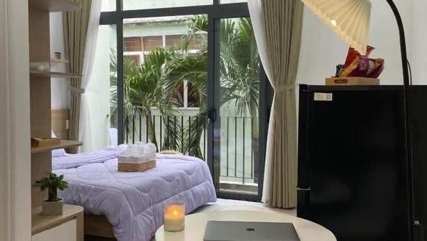 A modern bedroom with a bed, bedside table, lamp, and a view of the outdoors. - NHÀ TRONG NGÕ (Da Nang)