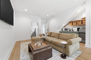 Una sala de estar moderna con un sofá seccional, una mesa de centro y una cocina equipada con microondas y refrigerador.