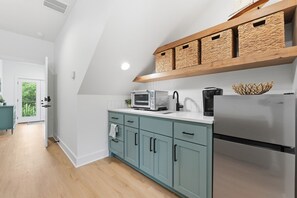 A modern kitchen with teal cabinets, a stainless steel refrigerator, a microwave, and a coffee maker. There is a wooden shelf above the counter with woven baskets. - Luxury Lakefront Escape on Beaver Lake - Sleeps the Whole Crew (Rogers)