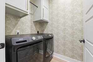A laundry room with two Maytag washing machines, a white door, and patterned wallpaper. - Luxury Lakefront Escape on Beaver Lake - Sleeps the Whole Crew (Rogers)