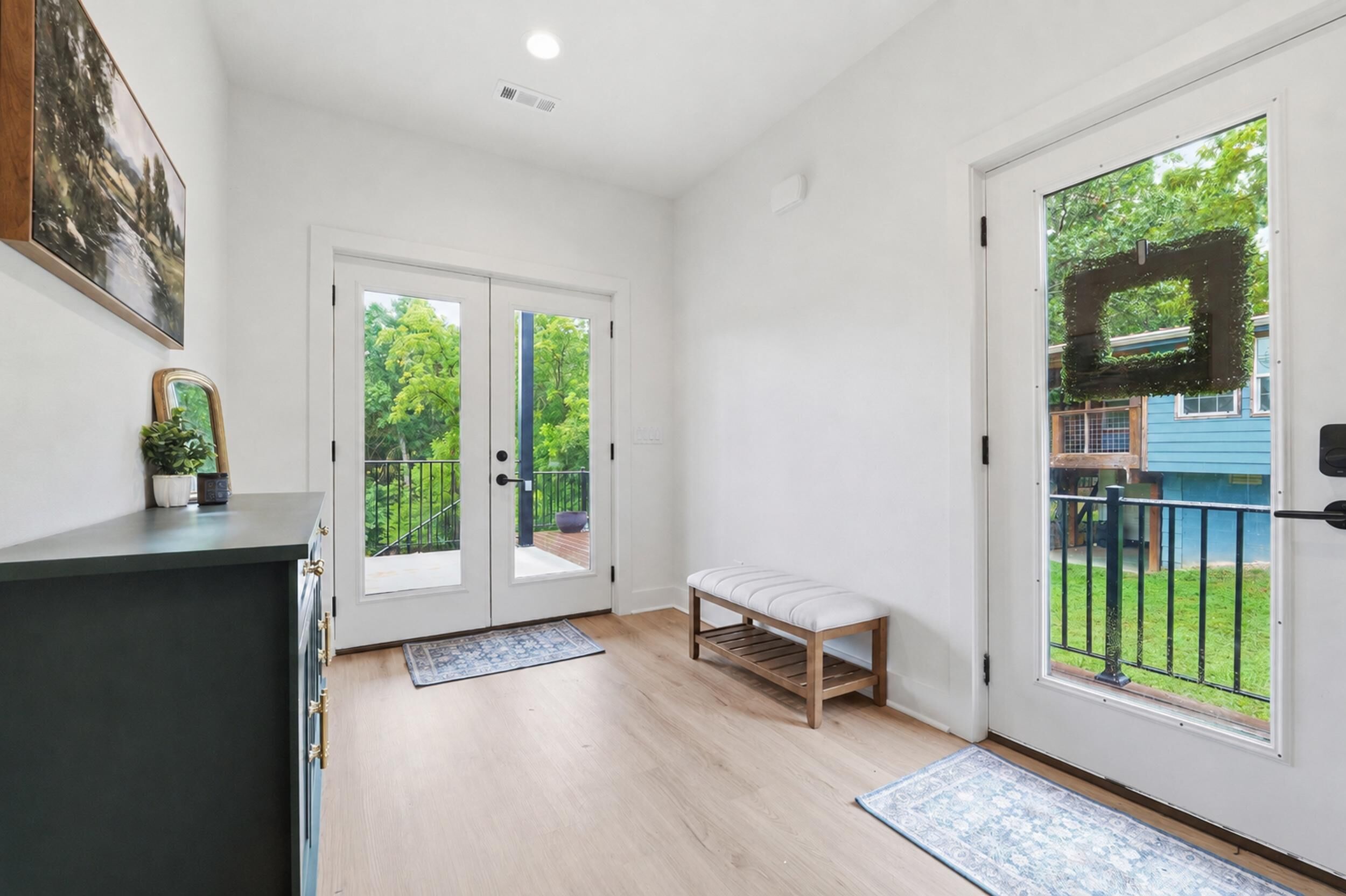 Ein heller, moderner Eingangsbereich mit Sitzbank, Doppeltüren zu einem Balkon und einem kleinen Topf mit Pflanze.