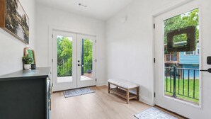 Ein heller, moderner Eingangsbereich mit Sitzbank, Doppeltüren zu einem Balkon und einem kleinen Topf mit Pflanze.