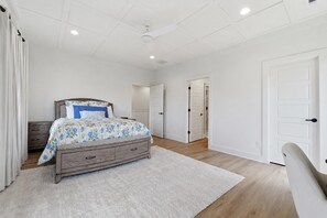 Un dormitorio con una cama, un aparador, una alfombra blanca y un ventilador de techo.