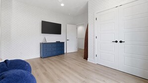 Ein Zimmer mit Holzboden, einem blauen Schminktisch und einem flachbildfernseher, der an der Wand befestigt ist, sowie weißen Türen.