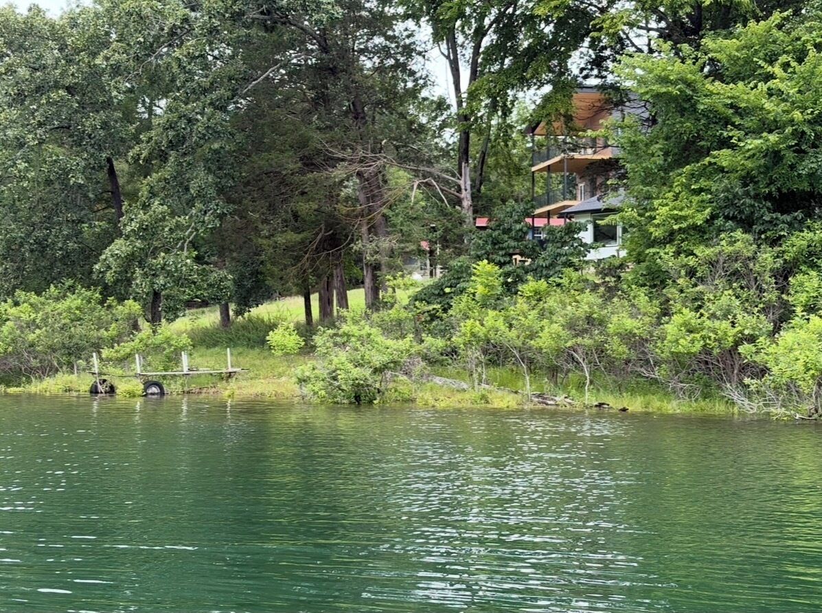 Une propriété au bord du lac, avec une maison entourée d’une forêt dense et une jetée qui s’avance dans l’eau.