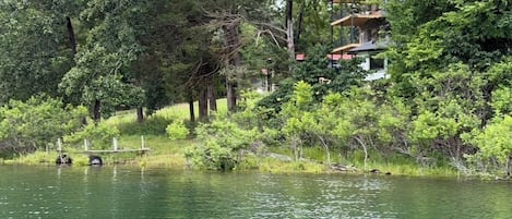 Une propriété au bord du lac, avec une maison entourée d’une forêt dense et une jetée qui s’avance dans l’eau.