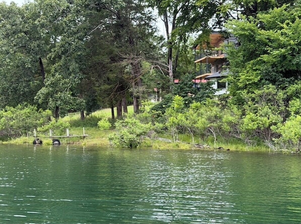 A lakeside property with a house surrounded by dense trees and a dock extending into the water. - Luxury Lakefront Escape on Beaver Lake - Sleeps the Whole Crew (Rogers)