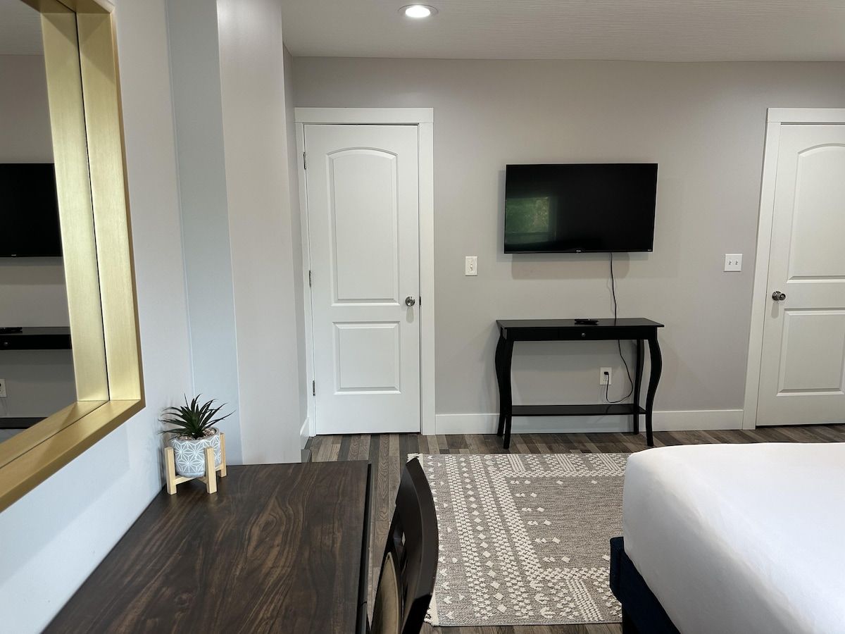 A hotel room with a bed, a TV mounted on the wall, a small table, and a potted plant.