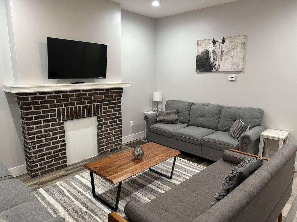 Un salon avec une cheminée, un téléviseur à écran plat fixé au-dessus, un canapé gris, une table basse en bois et un tapis à rayures.