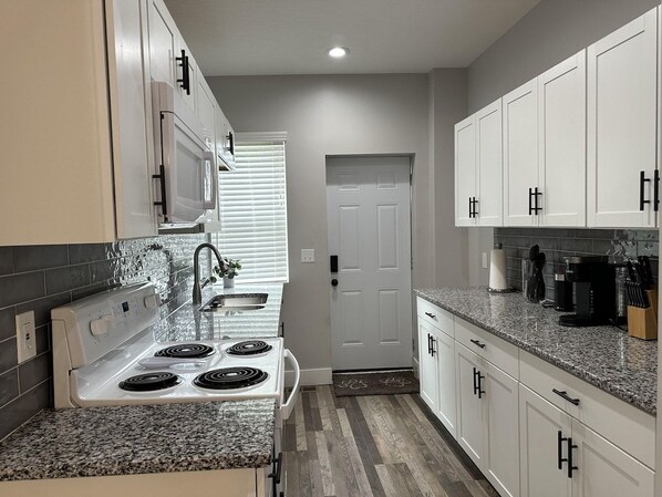 A modern kitchen with white cabinets, a granite countertop, a built-in microwave, and a stove.