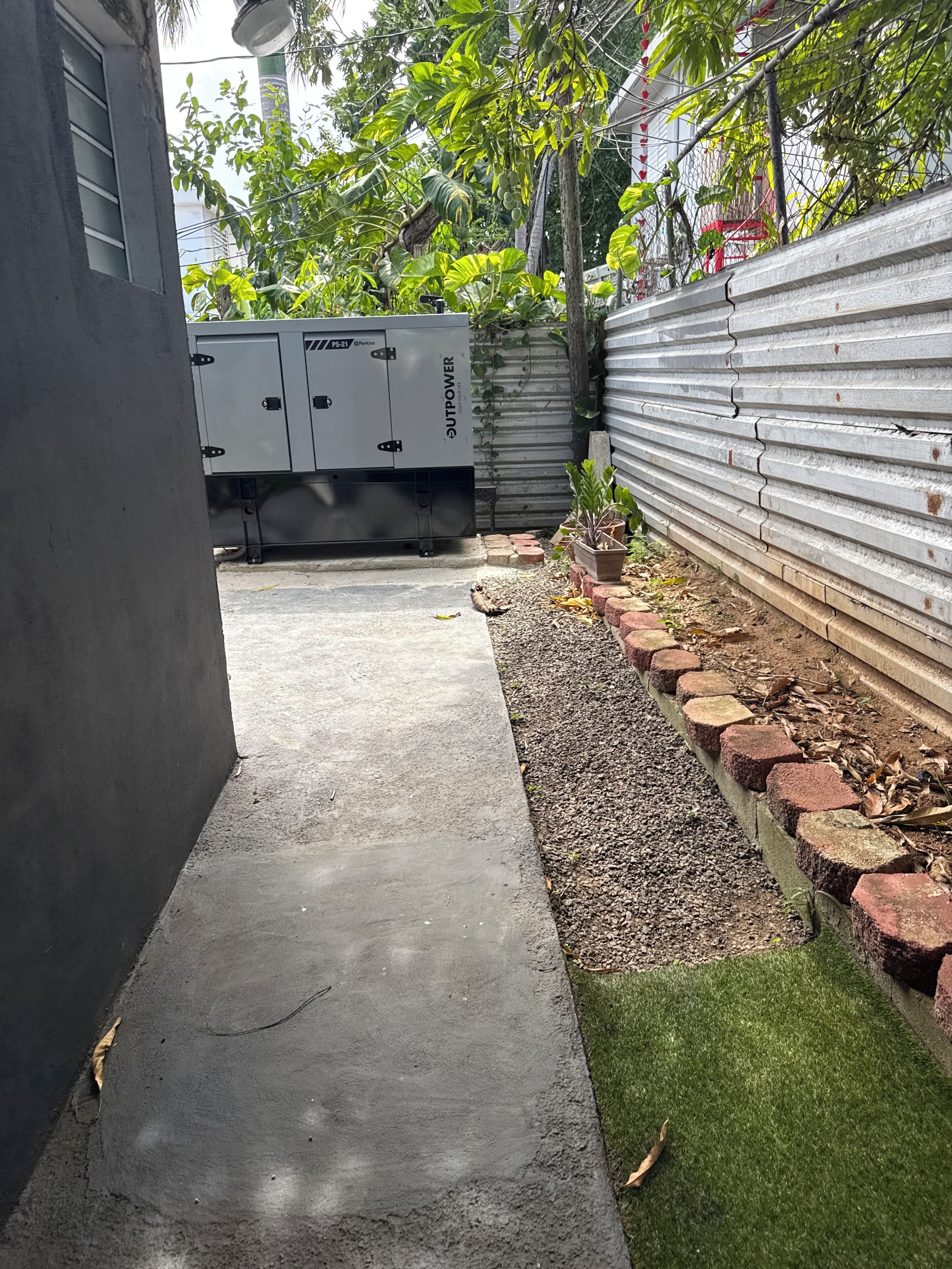 A concrete pathway leading to a gated area with a metal fence and vegetation.