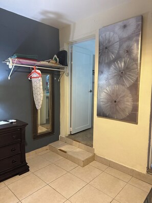 Una habitación con un aparador de color oscuro, un espejo de marco geométrico, una estantería montada en la pared con varios objetos y un cuadro abstracto de gran tamaño.