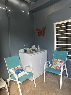 Eine kleine Küchenzeile mit Spüle und Schränken, zwei Stühle mit Blumenkissen und eine Schmetterlingsdeko an der Wand.