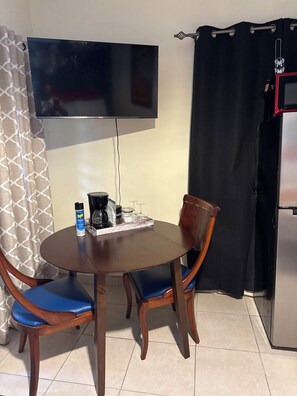 A dining area with a round table, two chairs, a television mounted on the wall, and a refrigerator. - 7 minutes from the airport (Carolina)