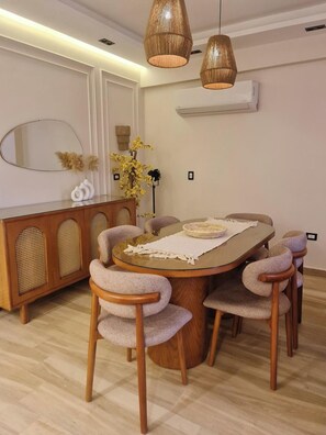 A dining area with a round table, six chairs, a wooden cabinet, and two hanging light fixtures. - 3-Bedroom Apartment with AC, Near Grand Egyptian Museum, Wasal Compound. (Cairo Governorate)