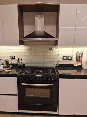 A kitchen with a stove, oven, and a range hood above the stove. - 3-Bedroom Apartment with AC, Near Grand Egyptian Museum, Wasal Compound. (Cairo Governorate)