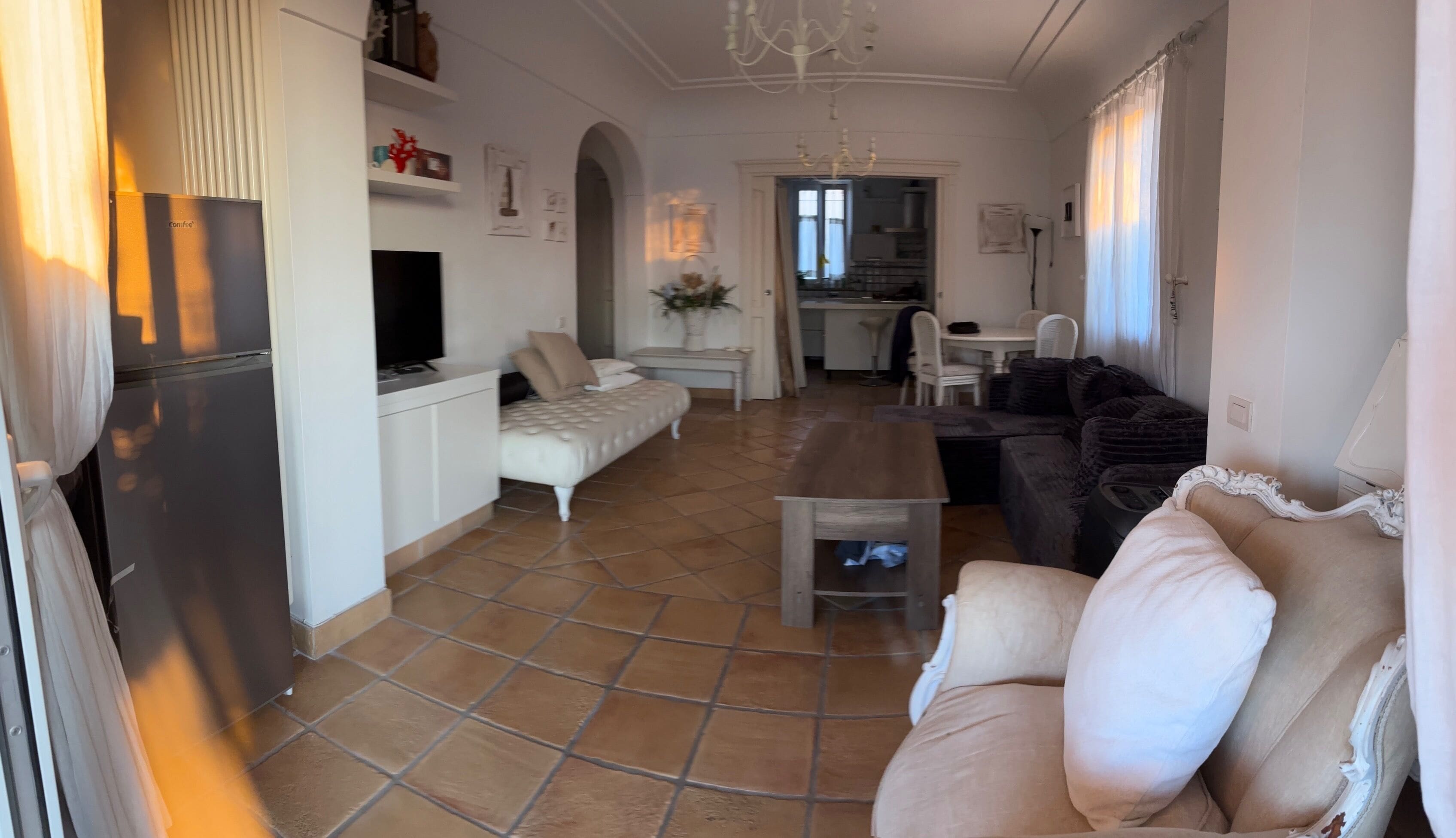 A living room with a sofa, a coffee table, a TV, and a kitchen in the background.