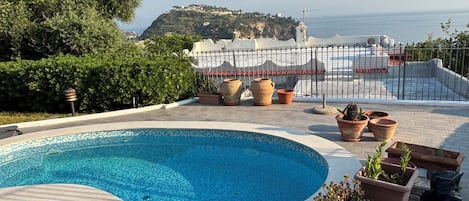 A swimming pool with a view of the sea and a mountainous landscape in the background.