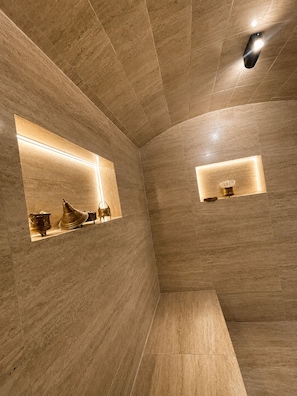 A modern bathroom with a curved ceiling, recessed lighting, and built-in shelves displaying decorative items.