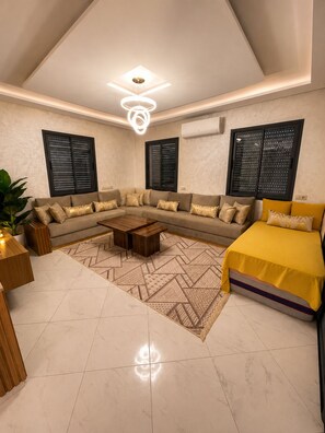A modern living room with a sectional sofa, a coffee table, and a bed with a yellow cover.
