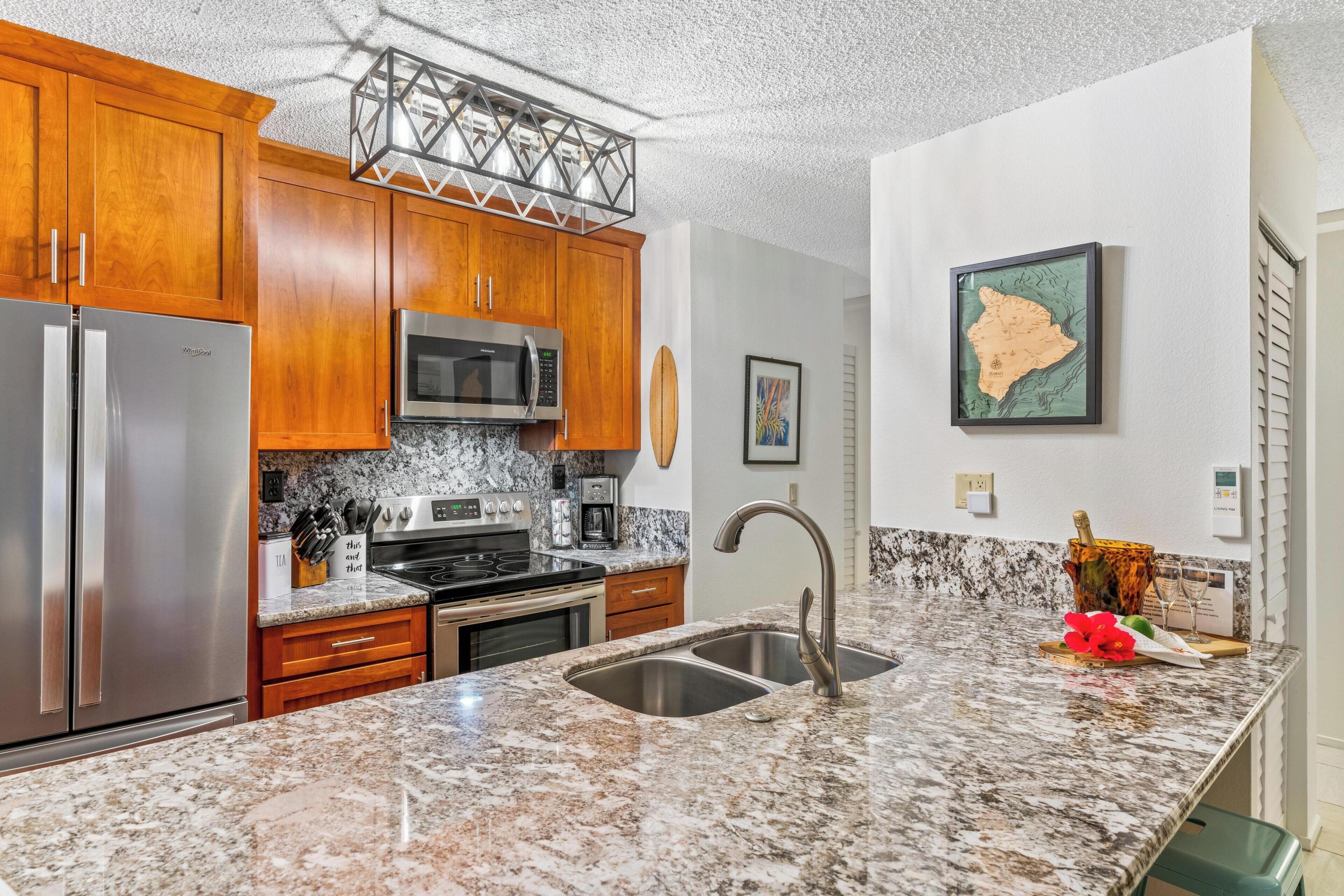 A modern kitchen with granite countertops, stainless steel appliances, wooden cabinets, and a large island with a sink.